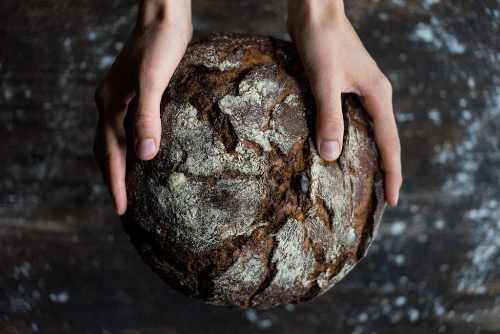 Close-up of hands holding a rustic loaf of whole wheat bread with a dark, textured crust.