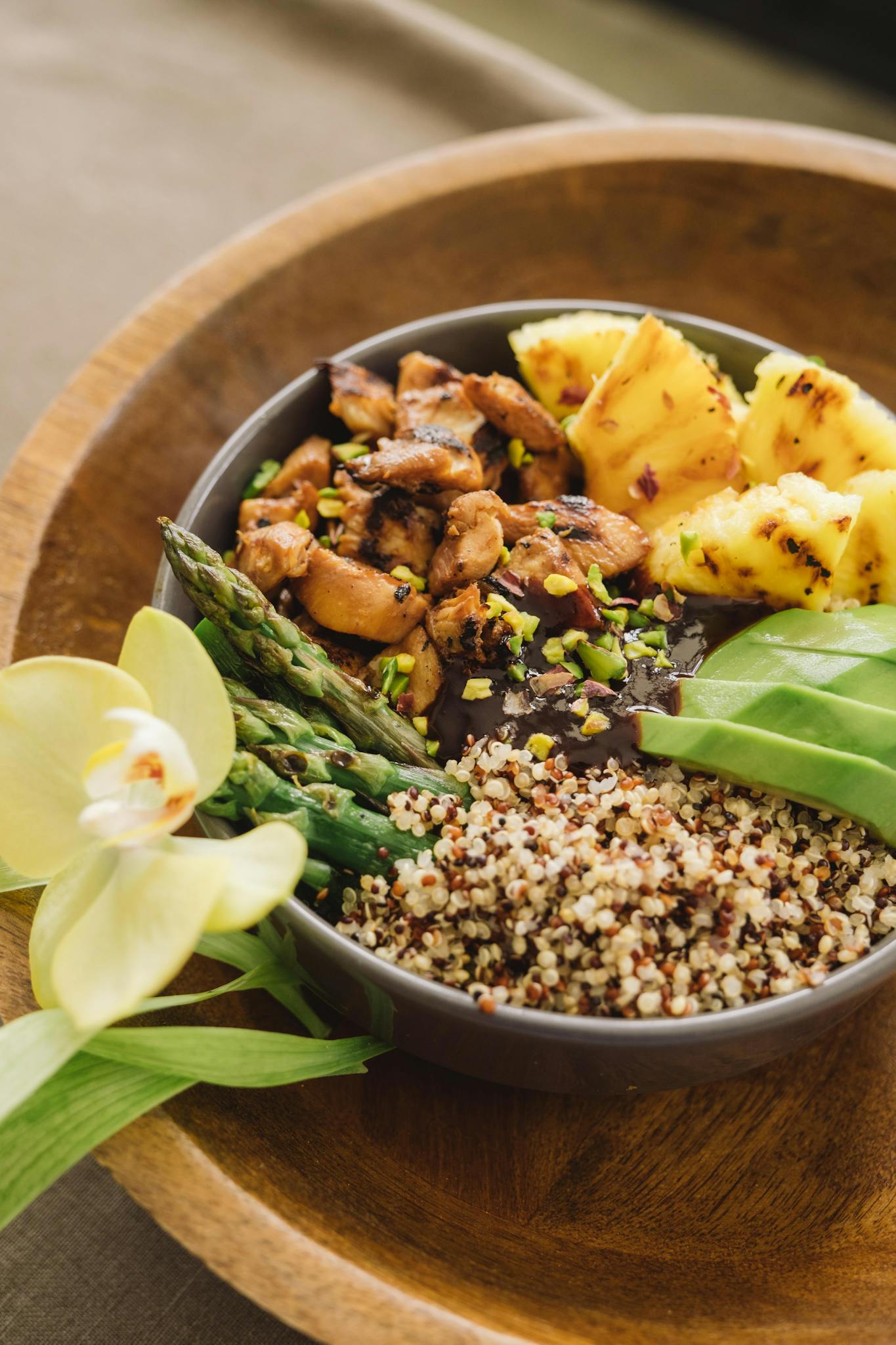 A vibrant quinoa bowl featuring grilled chicken, asparagus, pineapple, and avocado, beautifully presented.