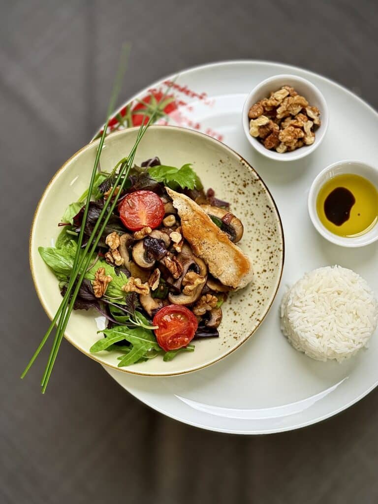 Mix Salad with Grilled Chicken and mushrooms on a large white plate. Served with Jasmin rice and seasoning ingredients.