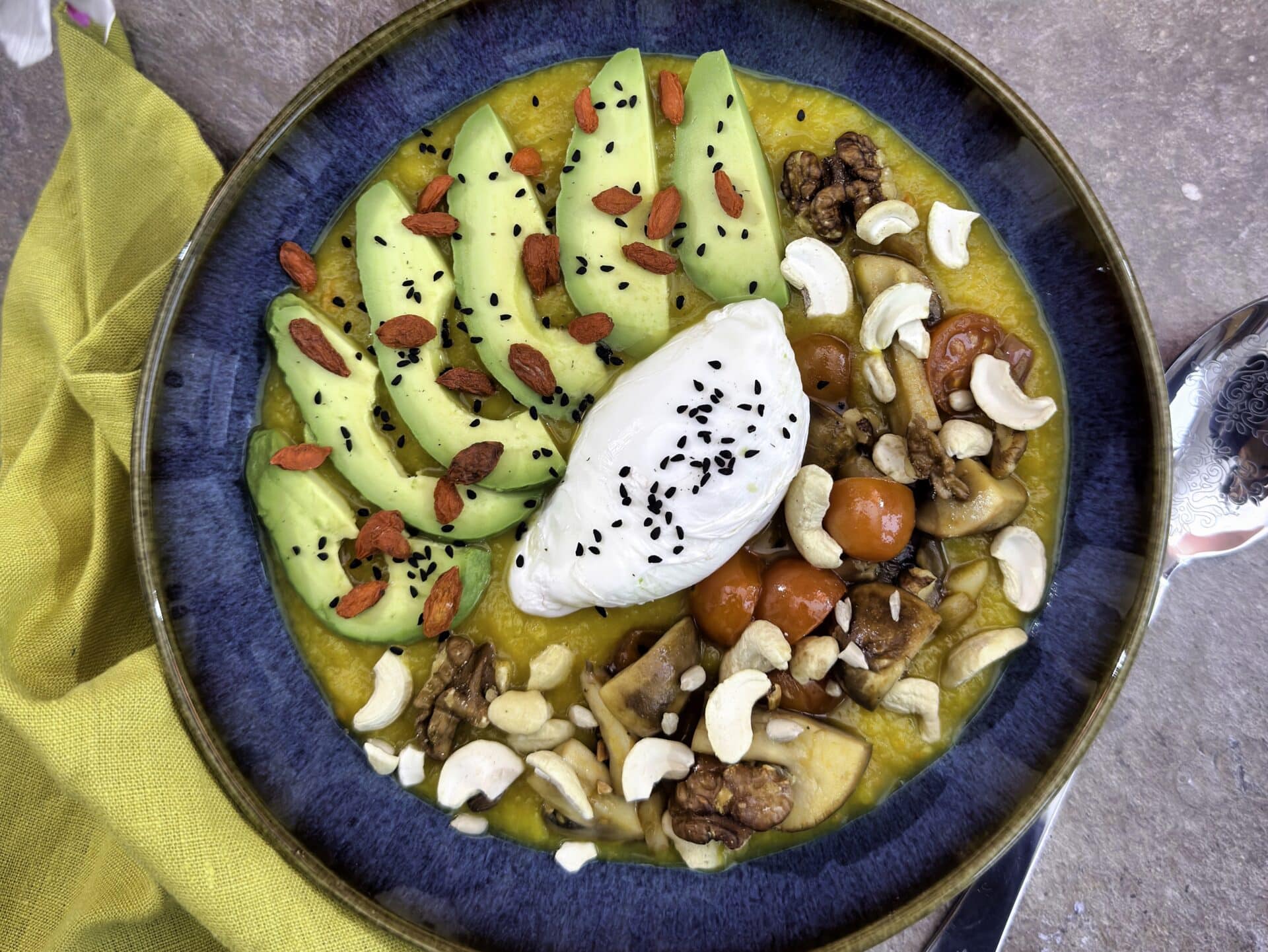 Roasted Pumpkin–Potato-Parsnip Velouté Bowl with Mushrooms, Tomato, Avocado & Poached Egg as topping, decorated with Goggi berries, nuts and black cumin.