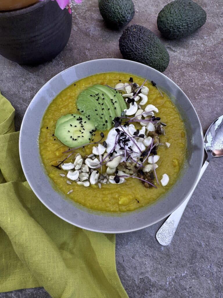 pumpkin, potato, parsnip veloute in a grey bowl, decorated with sliced avocado, black cumin, nuts and seeds