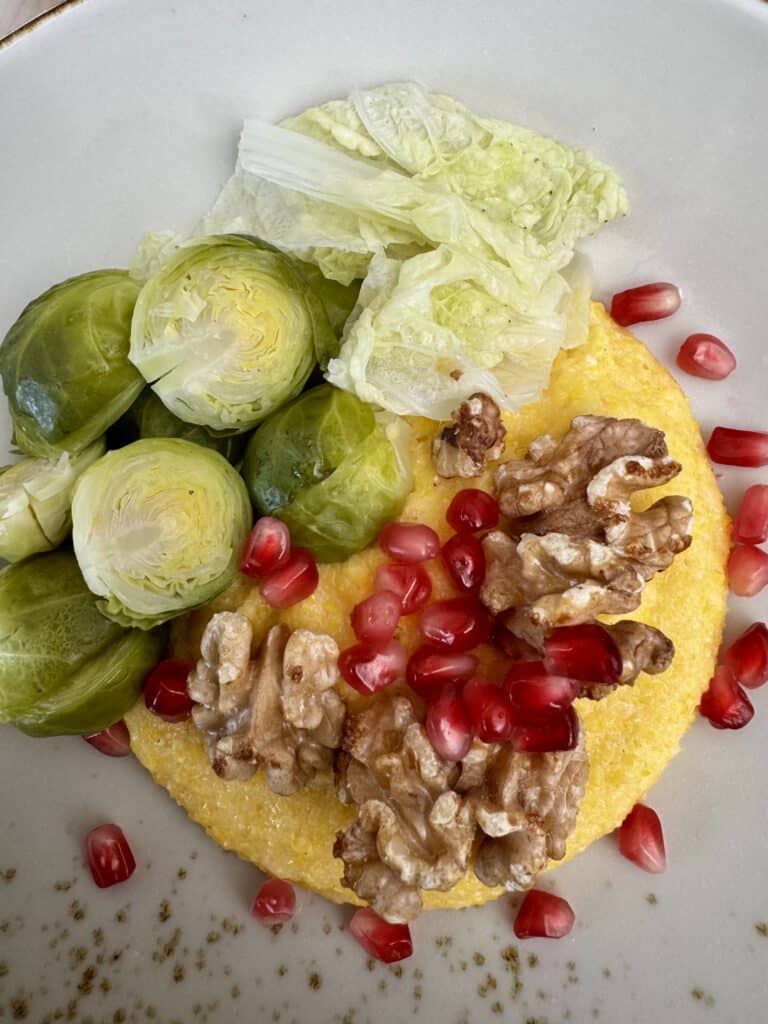 Close-up of steamed Brussels sprouts and Chinese cabbage served over creamy polenta, topped with walnuts and pomegranate seeds.