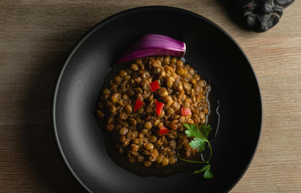 savory lentil dish garnished with onion and parsley in a black bowl.