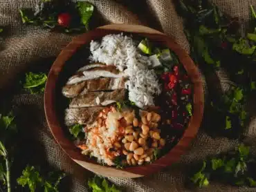 A wooden bowl filled with chicken, rice, and beans.