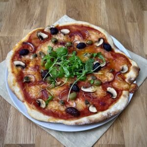 Overhead view of homemade wheat sourdough pizza topped with mushrooms, olives, capers, mozzarella and fresh rocket.