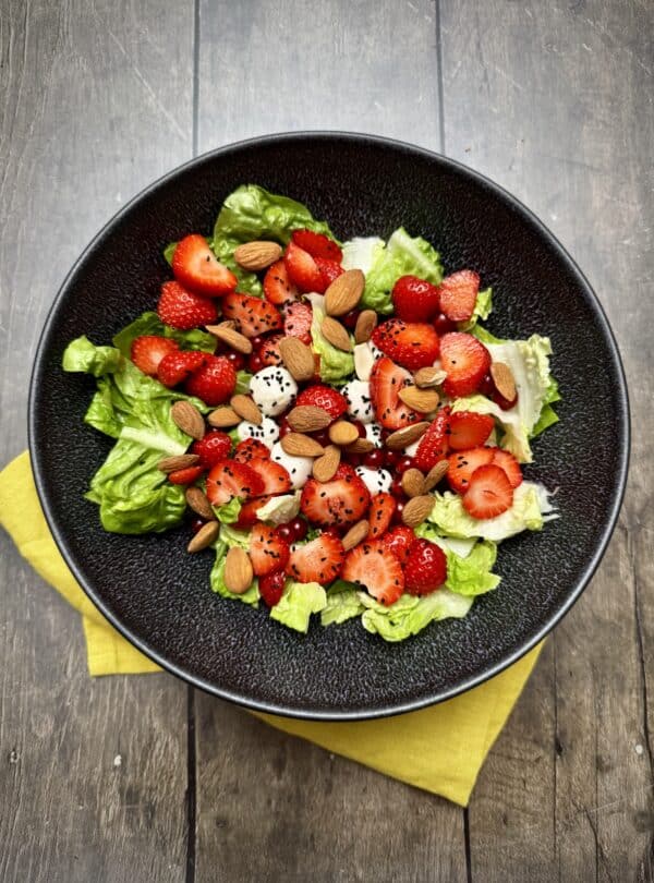 Top view of romana salad with berries, mozzarella and nuts arranged in a bowl.