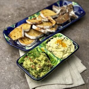 Side view of a snack plate with avocado dip and date yogurt dip served alongside slices of sourdough bread.
