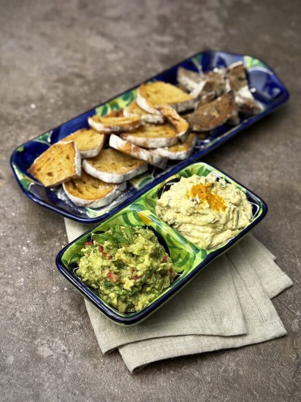 Side view of a snack plate with avocado dip and date yogurt dip served alongside slices of sourdough bread.