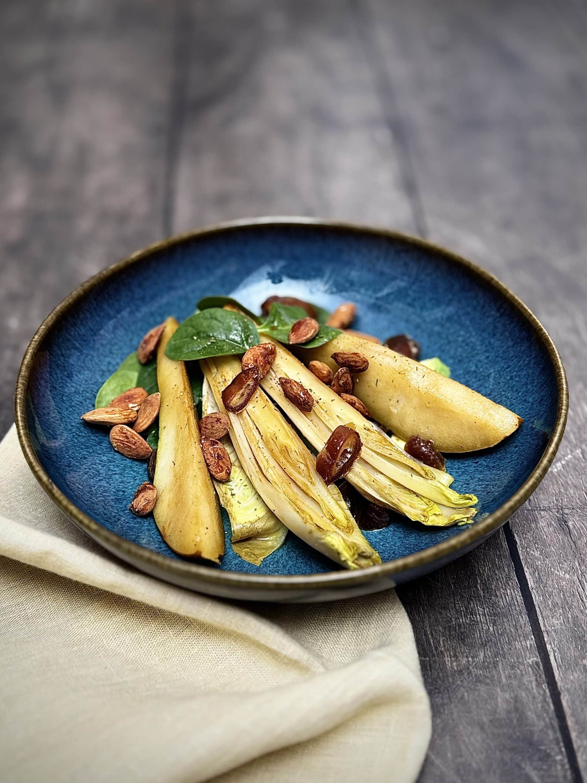 Caramelized pear, chicory, feta, avocado, and almonds in a blue salad bowl.