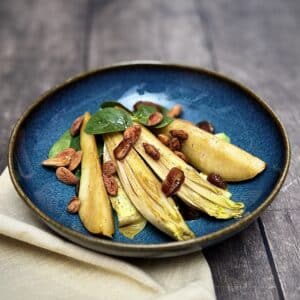 Caramelized pear, chicory, feta, avocado, and almonds in a blue salad bowl.