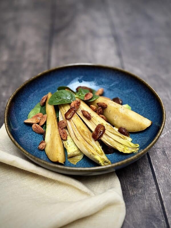 Caramelized pear, chicory, feta, avocado, and almonds in a blue salad bowl.