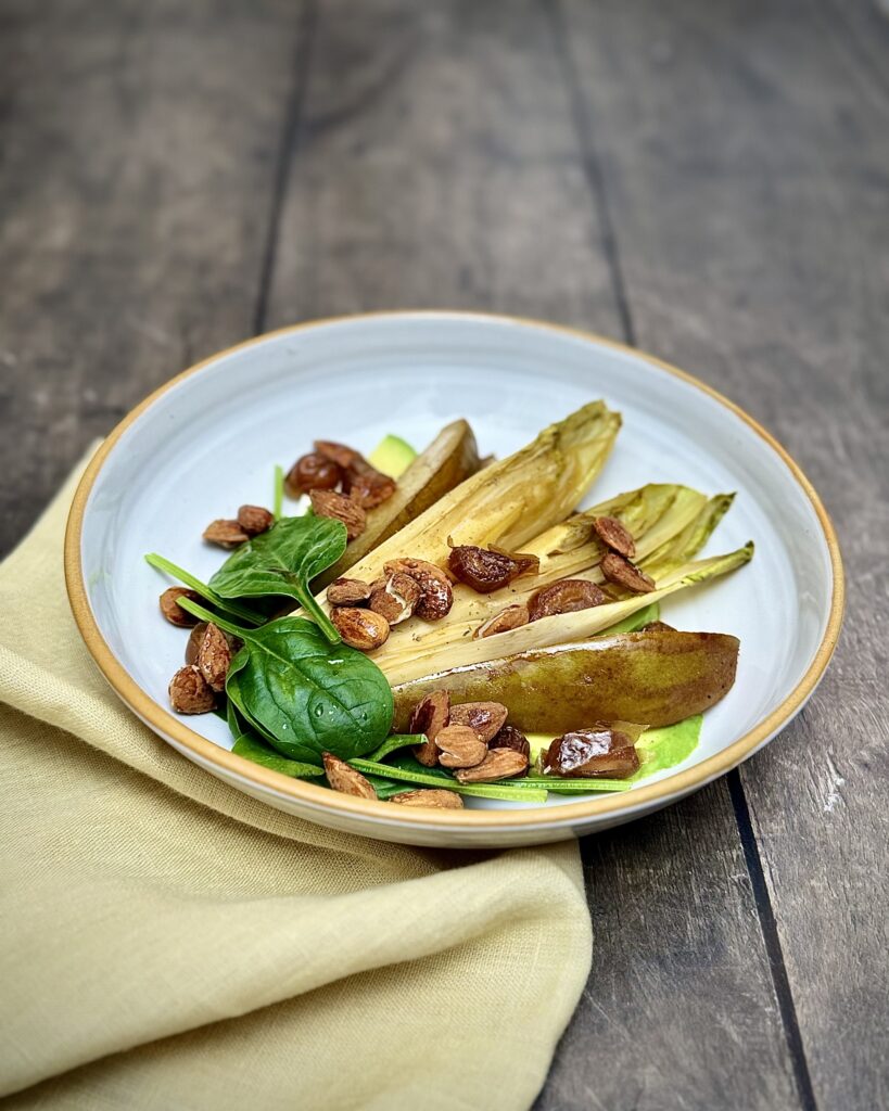 Caramelized pear, chicory, feta, avocado, and almonds in a white salad bowl.