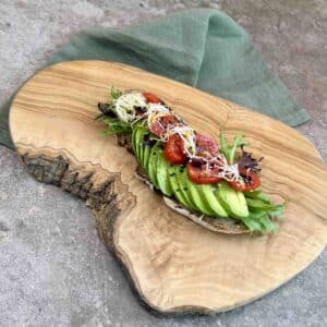 avocado sourdough toast topped with tomato sprouts salad leaves and sesame seeds on rustic wooden board