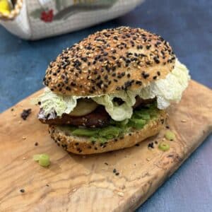 Crispy tofu burger with avocado, mushrooms, cucumber and Chinese cabbage served in a homemade sourdough sesame bun on a wooden board.