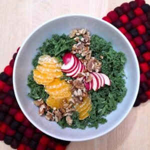 kale salad with orange apple and walnuts in a white bowl