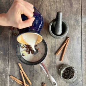 oat milk being poured over fresh turmeric ginger and spices for golden milk